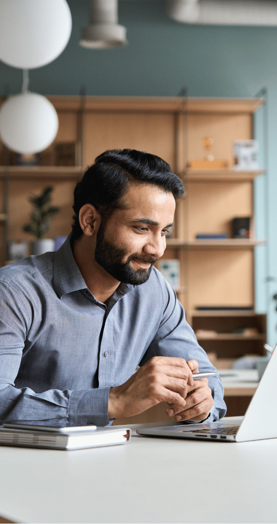 Young Adult Man Smiling Taking Notes while Learning on Computer